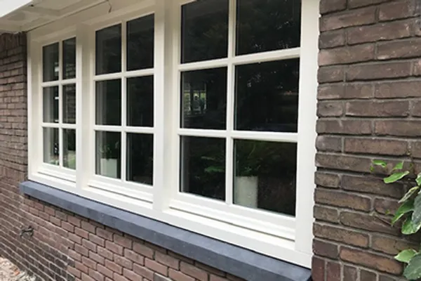 Detail van een wit kozijn met bakstenen gevel